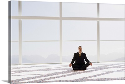 Man meditating, sitting cross-legged in office, eyes closed