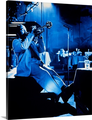Man sitting on edge of stage, playing trumpet