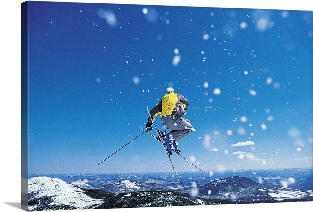 Photograph of man on skis in mid air jump over snow covered mountains.