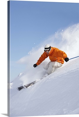 Man skiing down snow mountain slope sending up spray