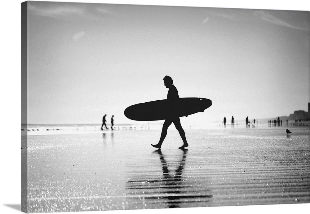 Silhouette of man walking with skateboard on beach.