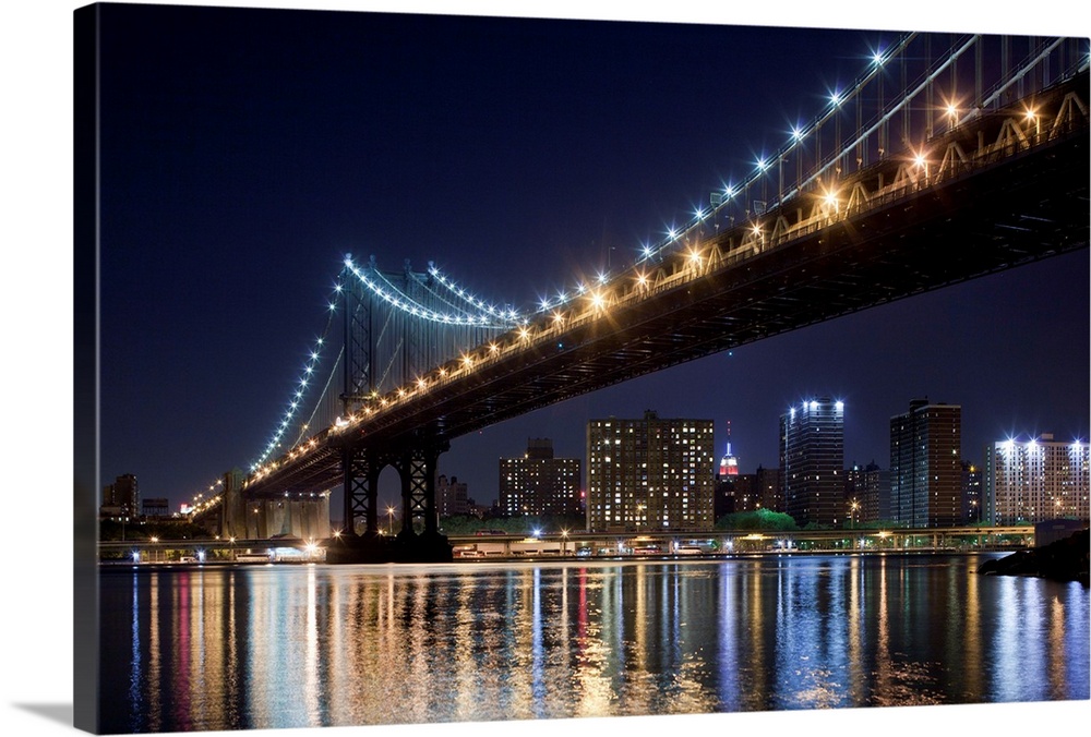 USA, New York, Brooklyn, Manhattan Bridge at night reflected in East River with Empire State Building glowing in distance