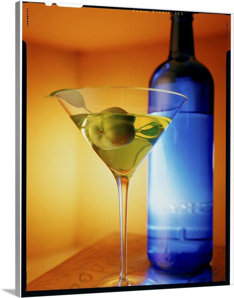 Big vertical photograph of fruit martini in a glass, sitting on a counter in front of a blue bottle.