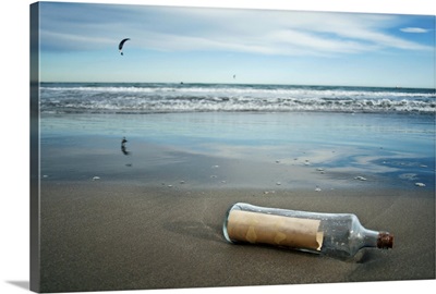 Message in bottle on beach, with reflection on sand an blue sky in background.