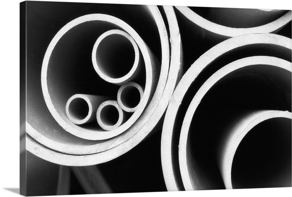 A stack of various sized metal  pipes stacked together photographed in black and white.
