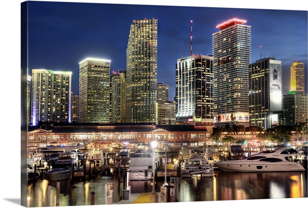 Photograph of the nighttime lit up Miami skyline down at the harbor with boats parked in their water slips.