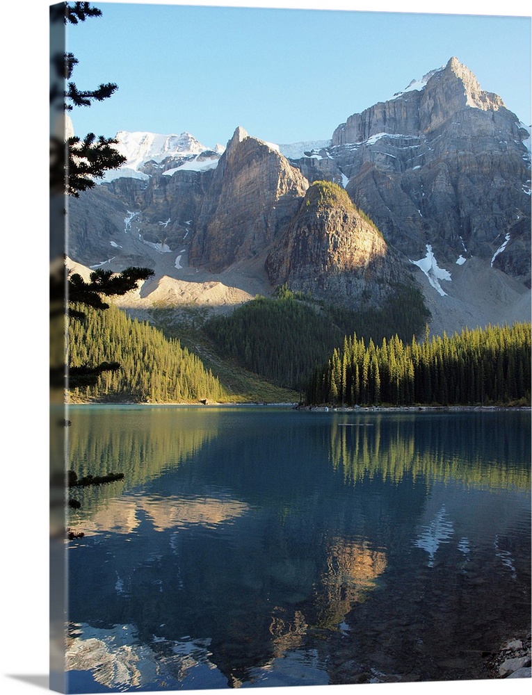 Snow-covered mountains and forest with a blue sky, reflected in Moraine Lake, a glacier-fed lake in Banff National Park in...