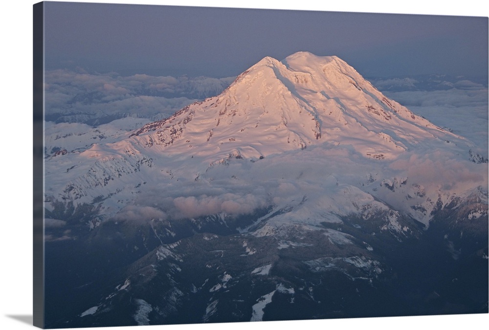Landscape, aerial photograph of a snow covered Mount Rainier, surrounded by clouds, a dark sky in the background, in Washi...