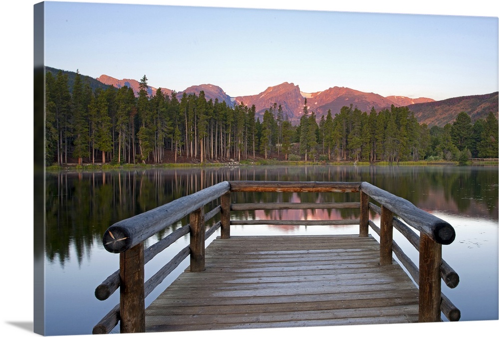 A picture taken from a small dock that sits on a lake and looks out onto a mountainous view and trees that line the other ...
