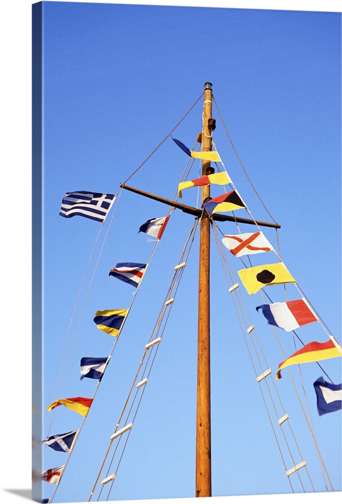 Multiple flags on the mast of a sailboat against a blue sky.