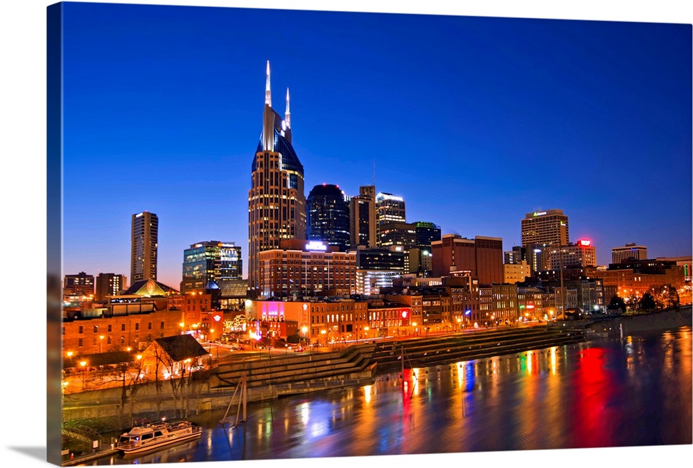 Big, horizontal photograph of the Nashville Tennessee skyline, lit up during blue hour, just after sunset, reflecting in t...