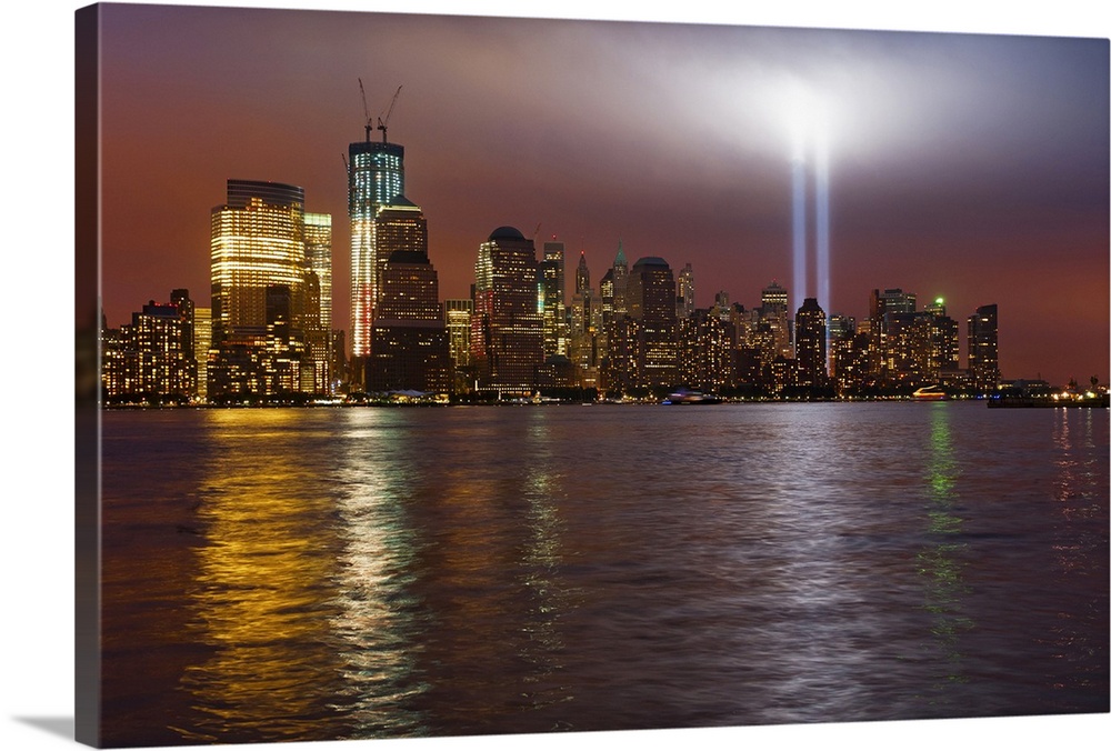Large, horizontal photograph of New York City, the Manhattan skyline at night, with 9/11 memorial lights.