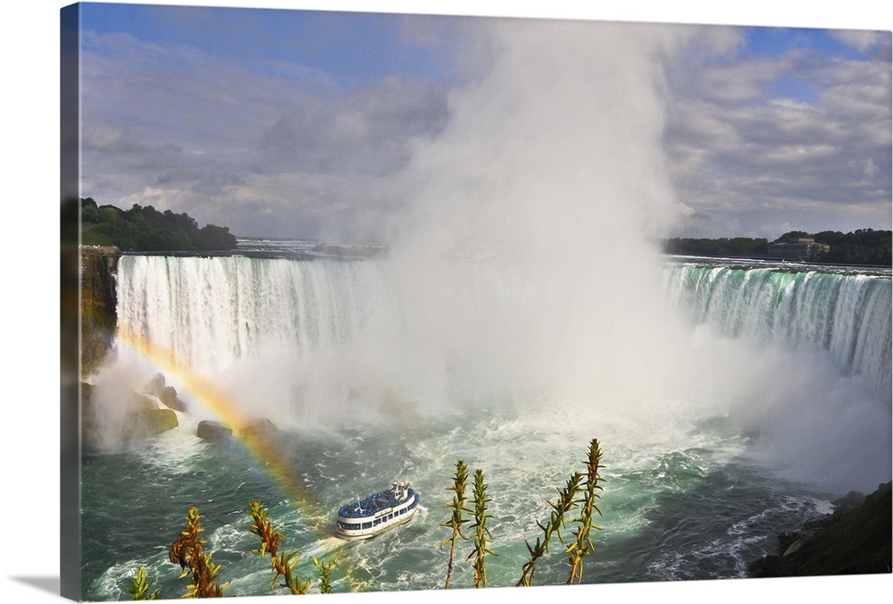 Wide landscape view of waterfall Rainbow in foreground Turquoise color of water Blue sky and white clouds.