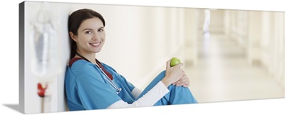 Nurse sitting with apple in hospital corridor