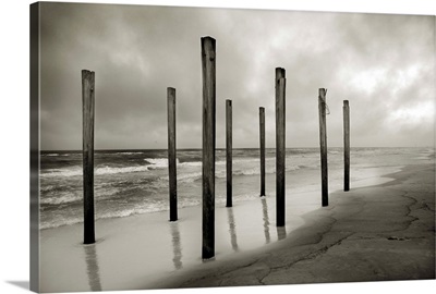 Old beach posts at the shoreline with clouds and ocean in the background.