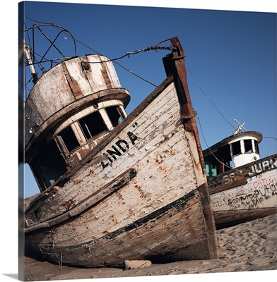 old neglected boats sit beached on sand under a blue sky