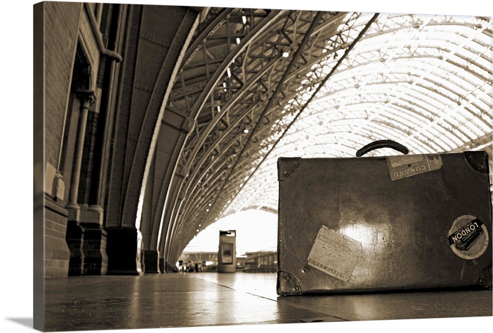 An old, sticker-bedecked suitcase under the Victorian canopy at St Pancras Station, London, England.