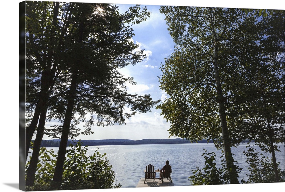 A 45 year-old woman sitting in an adirondack chair on a dock on Spencer Pond in Maine.