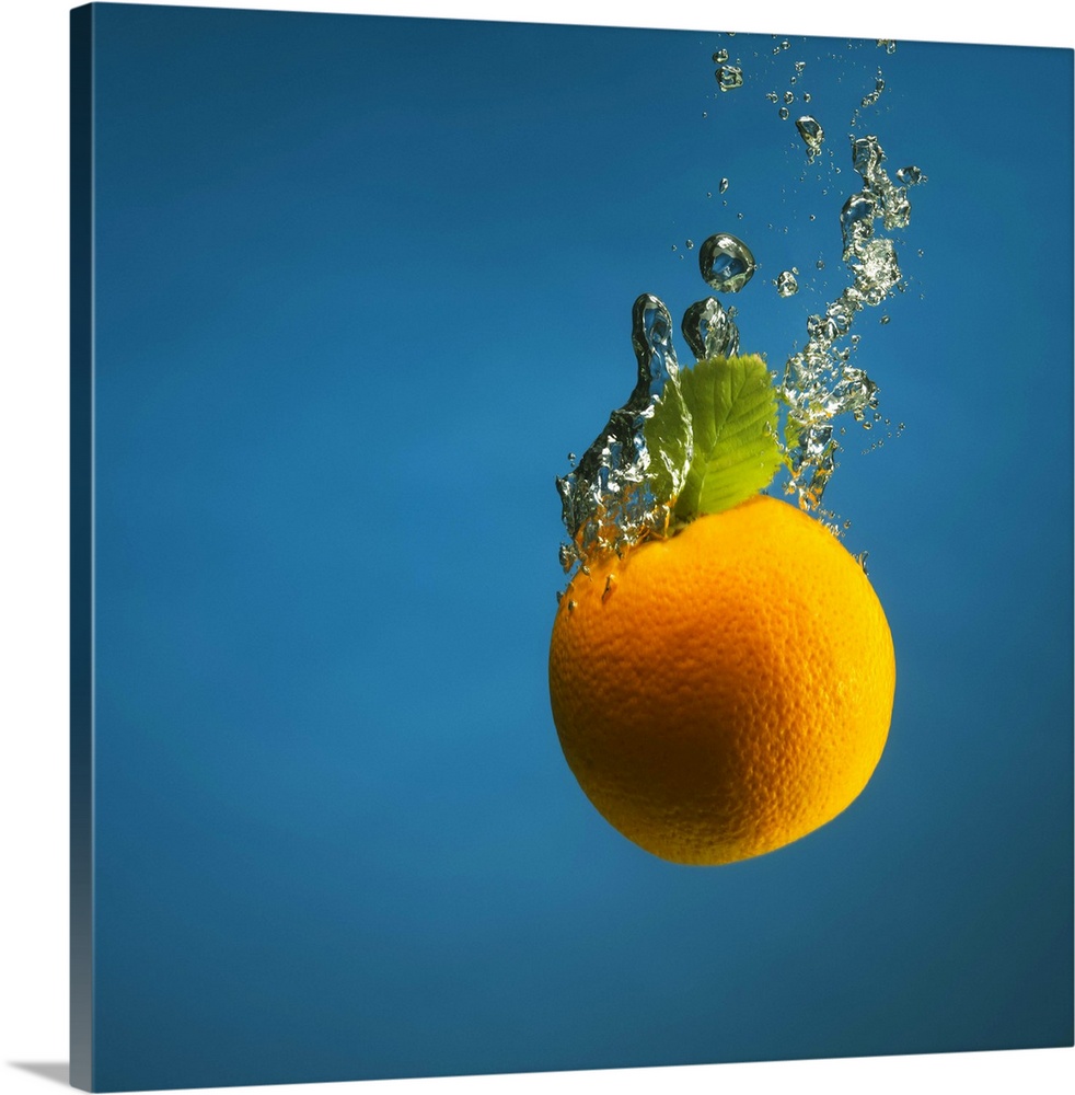 an orange splashed into water, creating bubbles, shot on blue backdrop