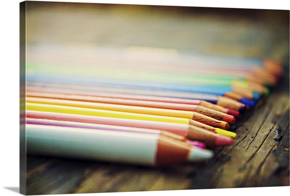 Row of colored pencils on rustic piece of wood.