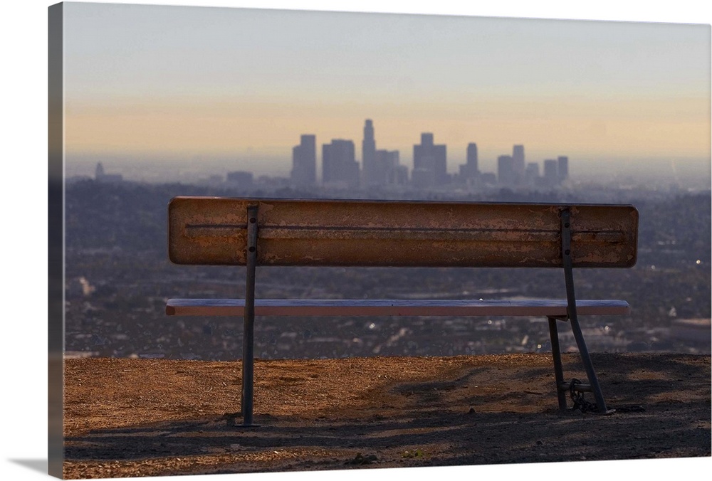 An empty and well-worn park bench over looking the downtown Los Angeles skyline.