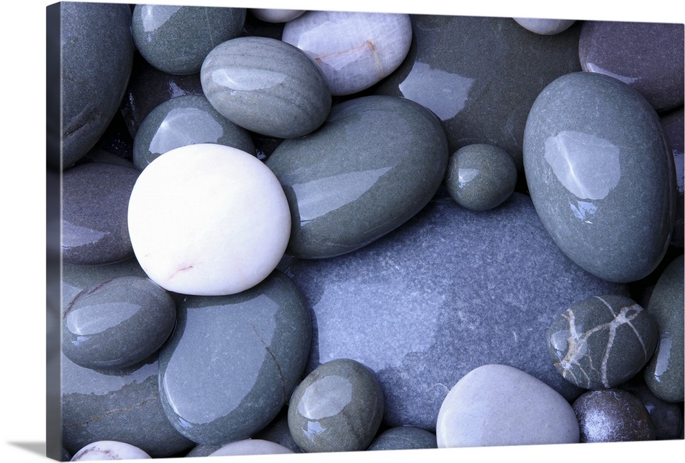 Close up photo of wet, smooth stones in varying oval shapes and gray colors.