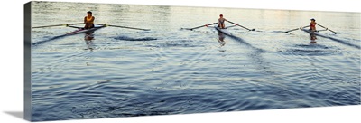 People rowing sculling boats on river