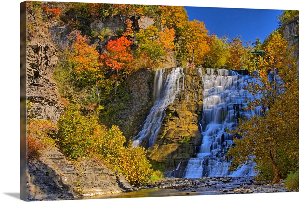 This large piece is of a sizeable waterfall that is surrounded by autumn colored trees and foliage.