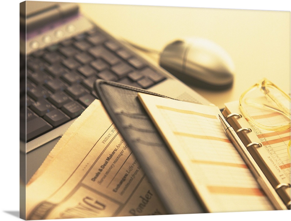 Personal organizer, glasses, newspaper and laptop on desk, high angle view, close up, soft focus