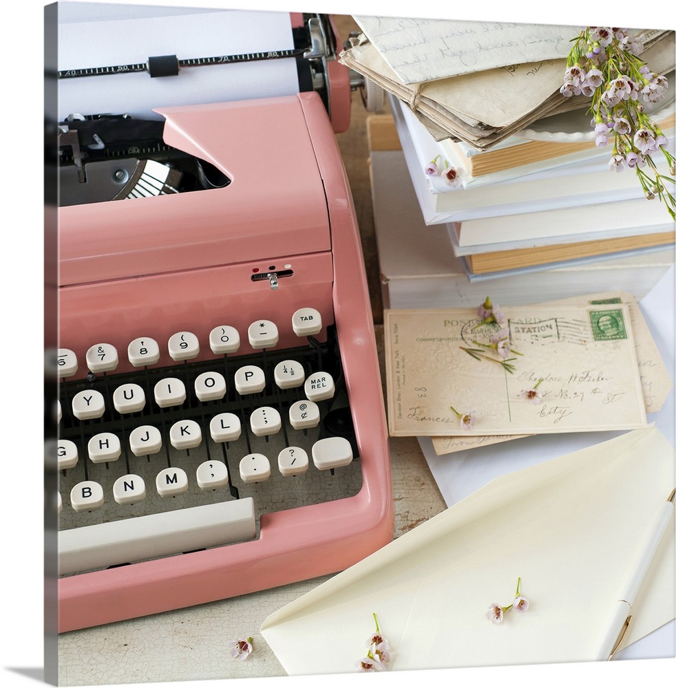 A pink typewriter surrounded by old books, letters and dried flowers in this square shaped, decorative photo art.