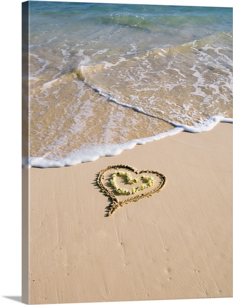 Picture of a heart drawn in the sand on a tropical beach, yellow lei shaped like a heart inside of drawing