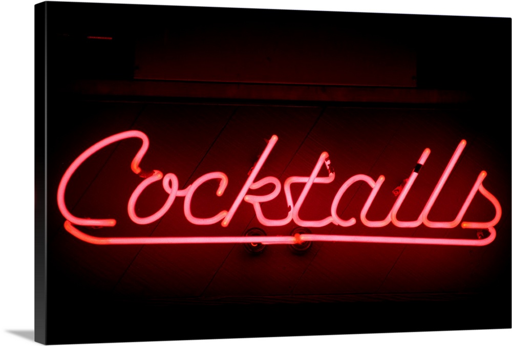 An illuminated pink sign with the work cocktails sits on a dark wall.