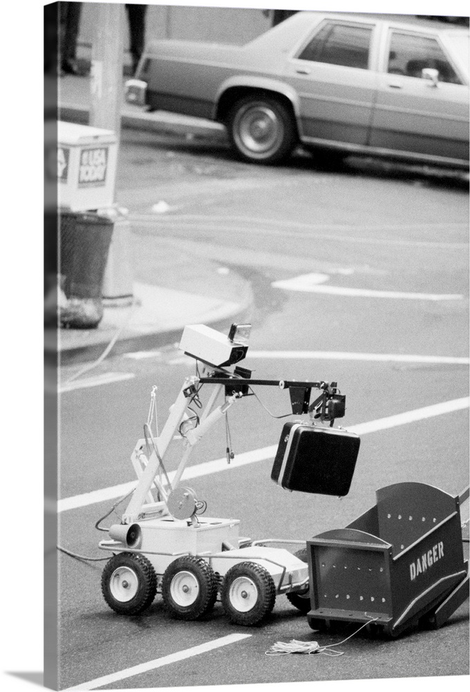 A police bomb squad robot carries a suspicious attache case to a disposal box in the middle of the street. The case was fo...