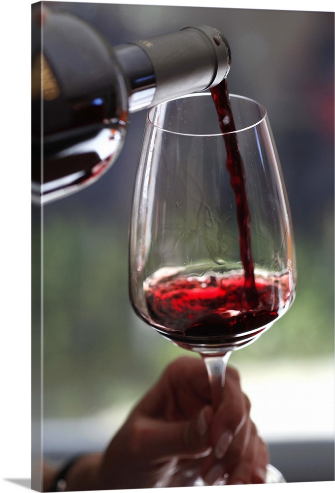 A woman pouring a sampling of red wine at a wine tasting, focus on hands