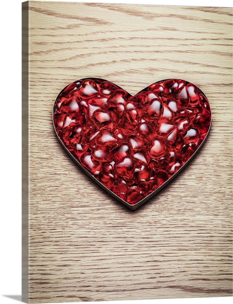 A mass of plastic red hearts sit in a heart shape on a wooden background