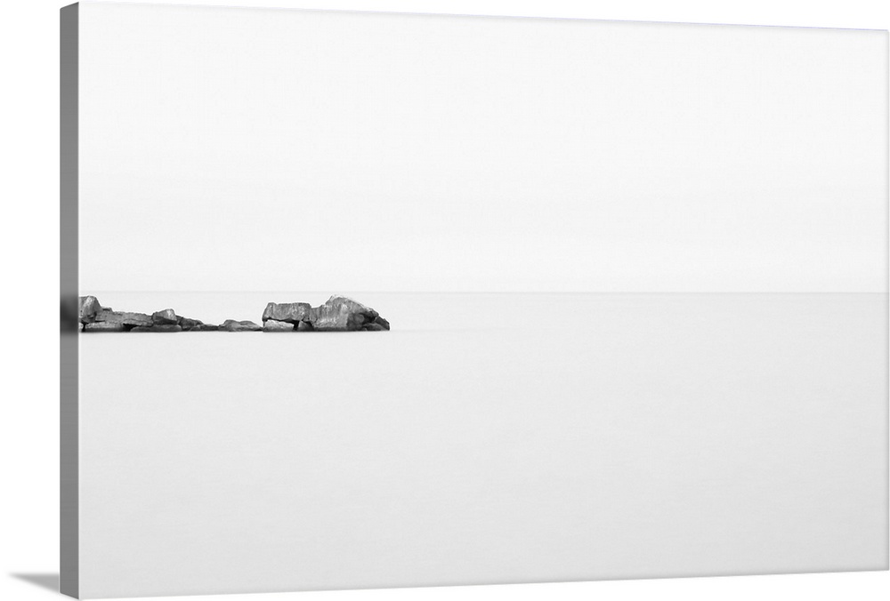 Black and white photograph of a rock breakwater jutting out into the glass-like water of Lake Huron on an overcast morning.
