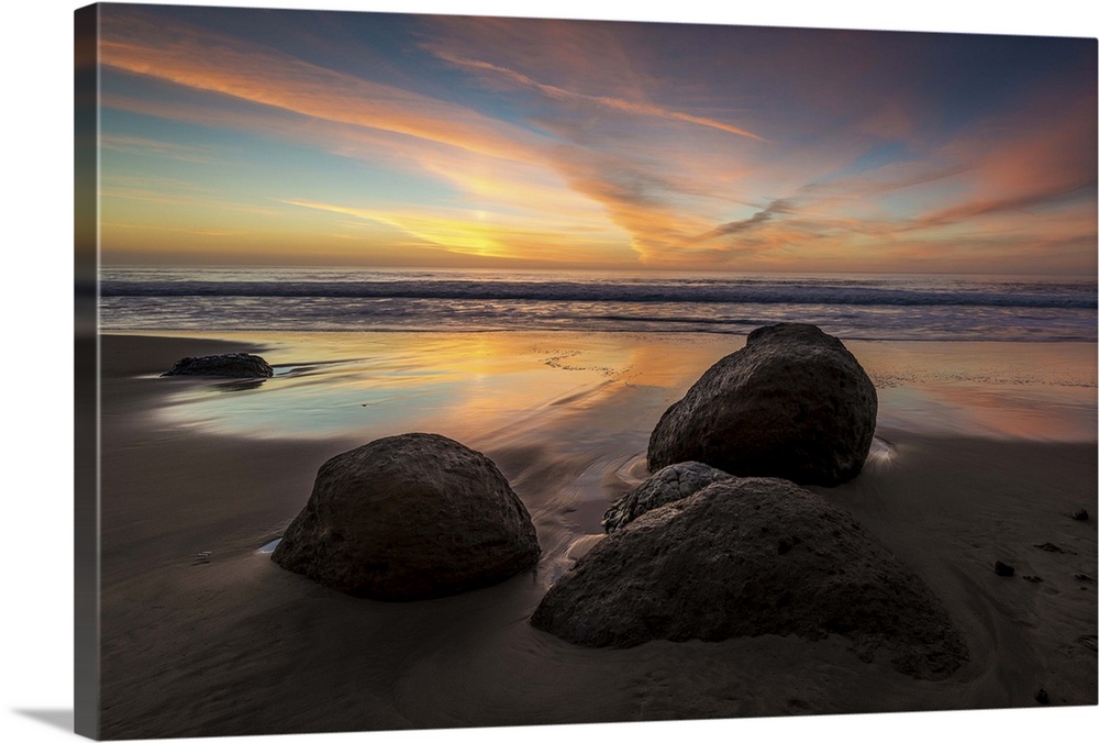 Rocks on a beach in the foreground and a colorful sunset in the background.  Pomponio State Beach in San Gregorio, Califor...
