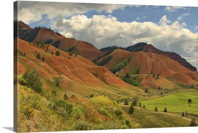 Rolling red hills under a cloudy blue sky during the summer in rural Wyoming