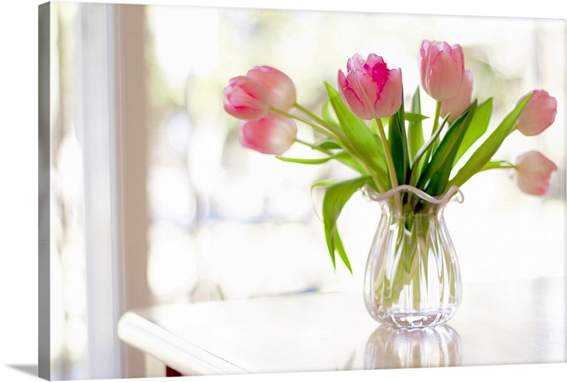 Ruffled pink glass vase filled with soft, pink tulips in front of ...