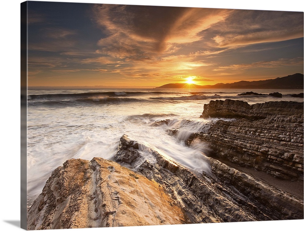 Dramatic sunset with chiseled rocks and amazing cloud formations. Waves are breaking over rocks in foreground.