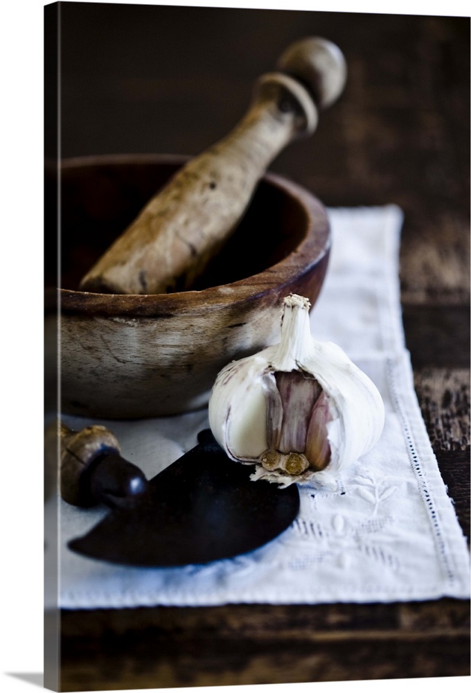 Rustic garlic crucher and clove of garlic on rustic table vintage lace tablecloth.