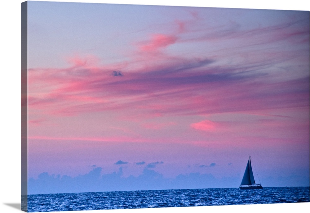 Feathery clouds, colored red from the sunset, over a blue sea with a sail boat
