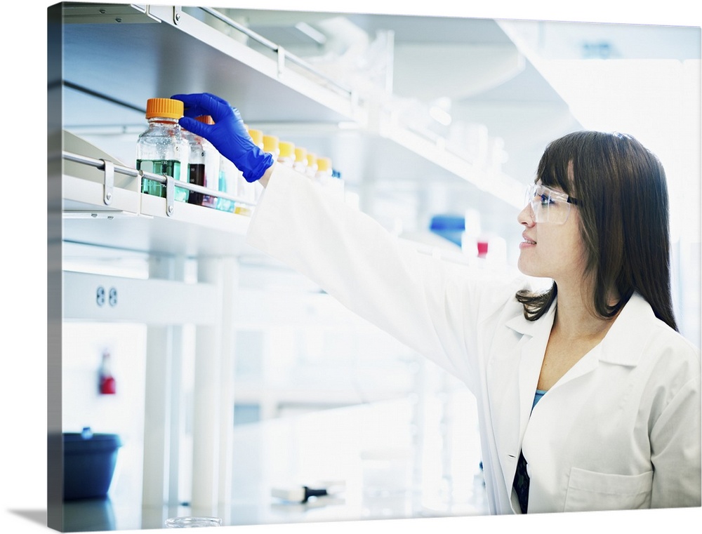 Smiling scientist reaching for bottle of solution in research laboratory