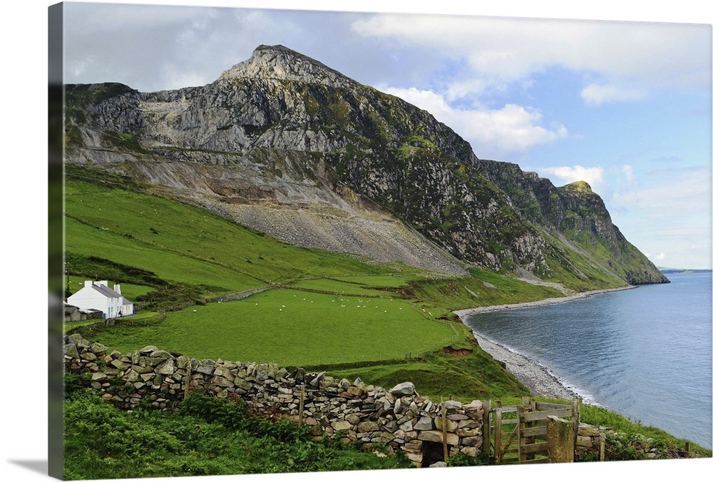 Seascape of coast path at Trefor on Lleyn Peninsular in North Wales which includes cottage, beach and mountains on sunny day