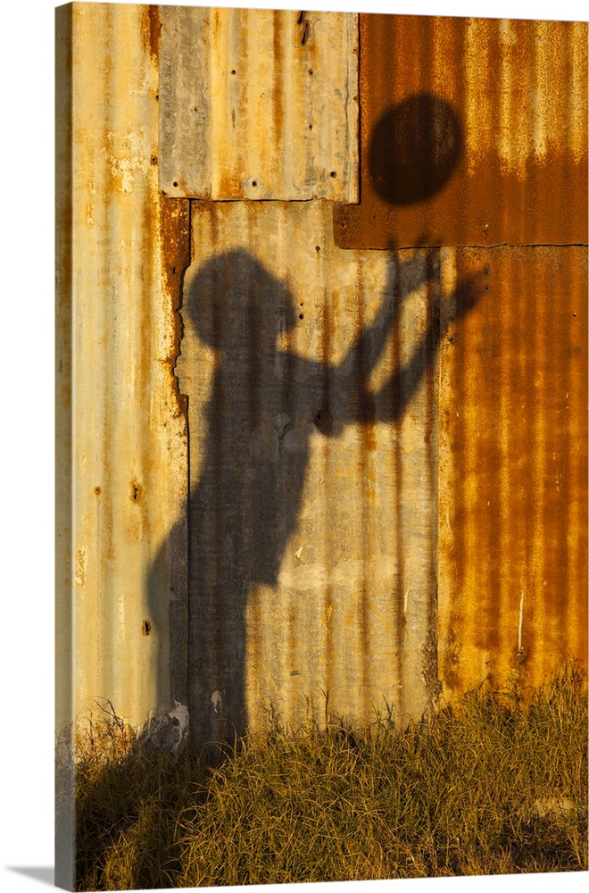 Shadow of a young rugby player throwing a ball, silhouetted on a corrugated iron fence at Arniston.