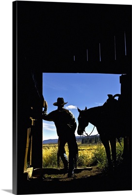 silhouette of a cowboy holding his horse's reins and looks out of the barn
