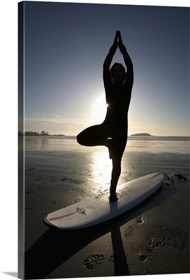 silhouette of female surfer doing yoga tree pose