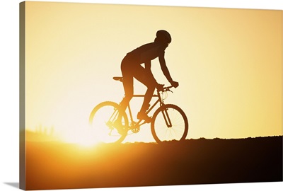 Silhouette of man riding mountain bike at sunset