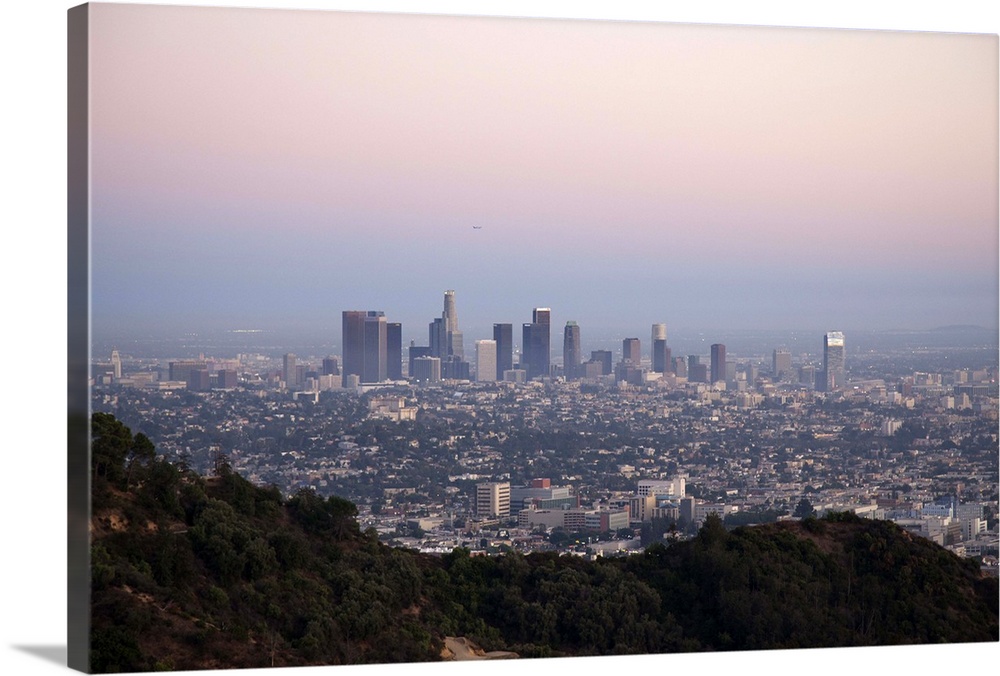 Landscape view of skyscrapers of downtown LA with hills of Griffith Park in foreground as seen at sunset