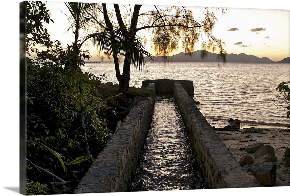 Small canal flowing into the Indian Ocean at sunset, in a tropical setting. The stream of water runs between a sandy beach...